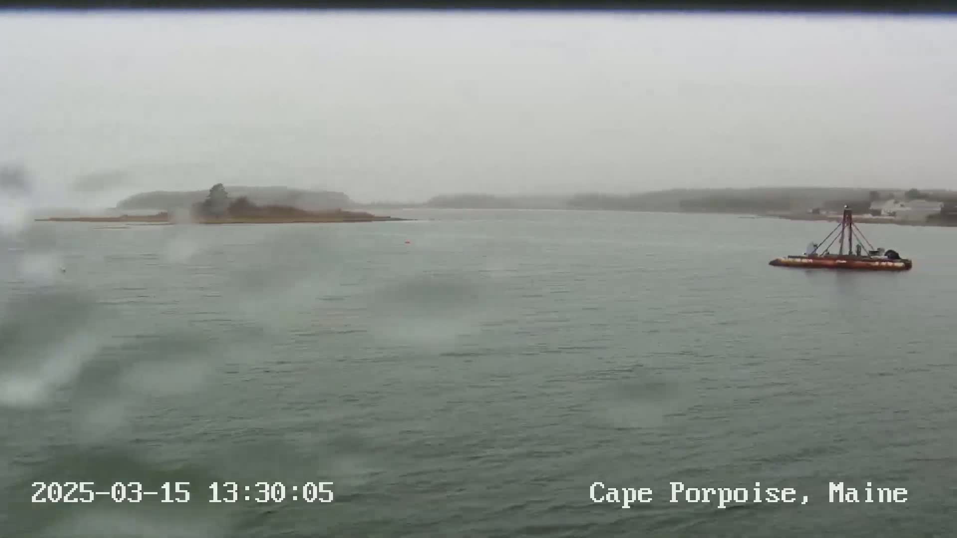 A small barge sits on a body of water in foggy conditions, with a small island visible in the distance.