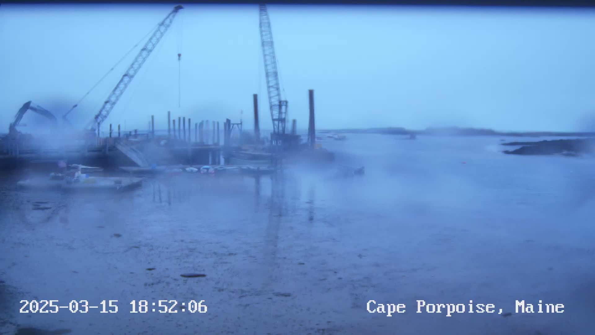 Construction cranes and equipment sit on a foggy waterfront.