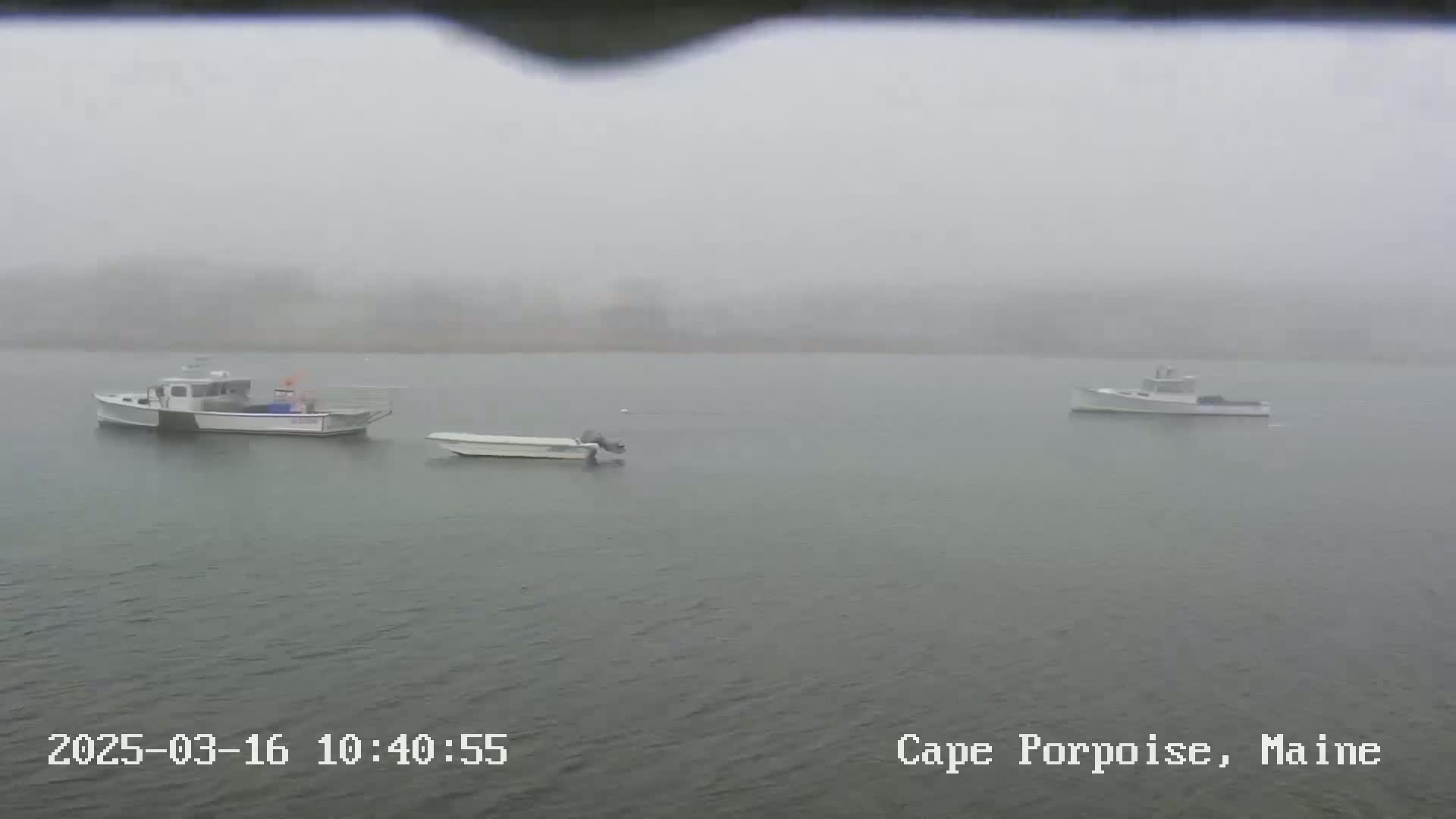 Three small boats are moored in a foggy body of water.