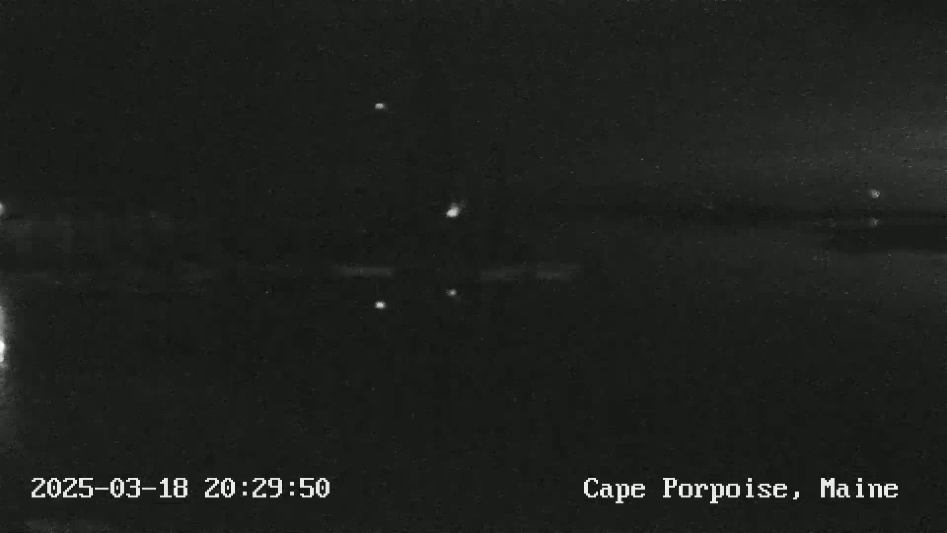 A nighttime, low-light image shows a dark body of water with a few small, bright lights visible on the surface.