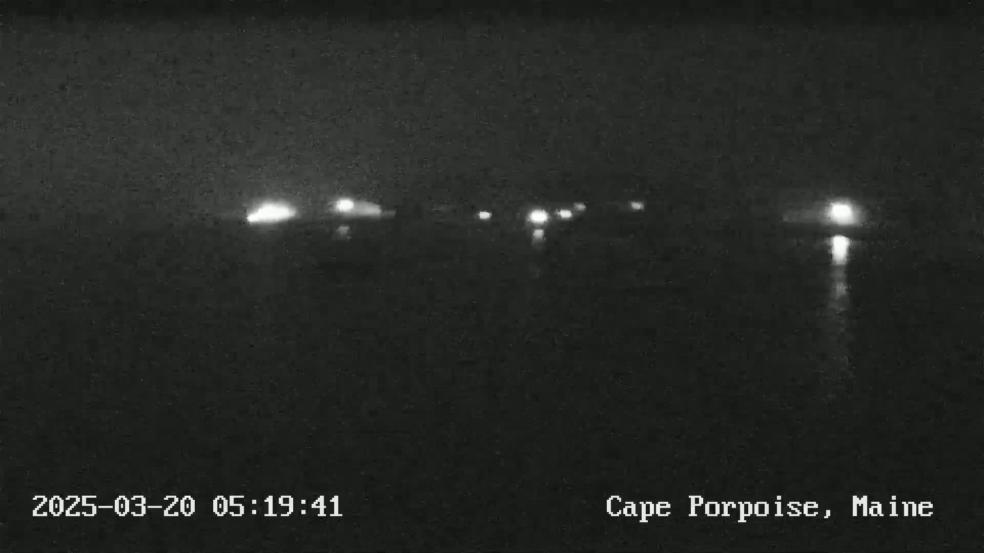 A nighttime, low-light view of a dark body of water with faint lights visible in the distance.
