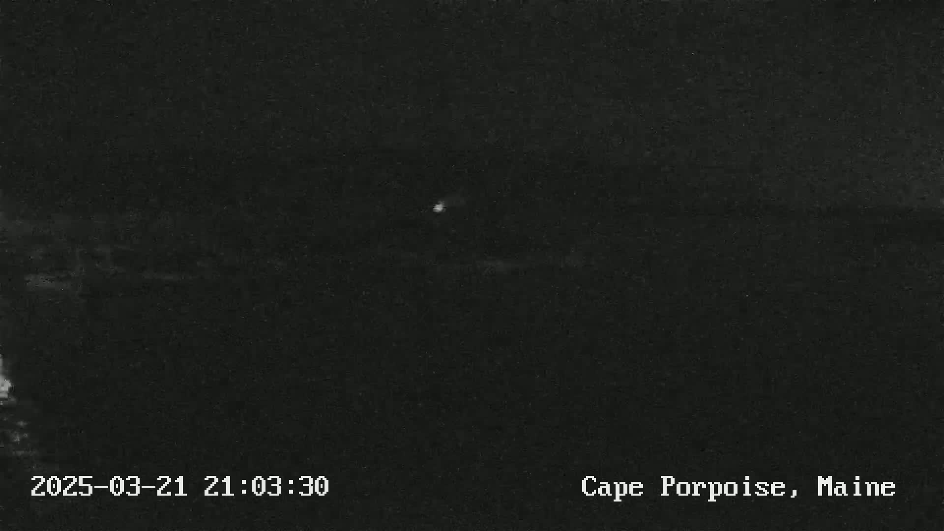 A dark, nighttime image shows a dimly lit area, possibly a body of water, under a clear sky.