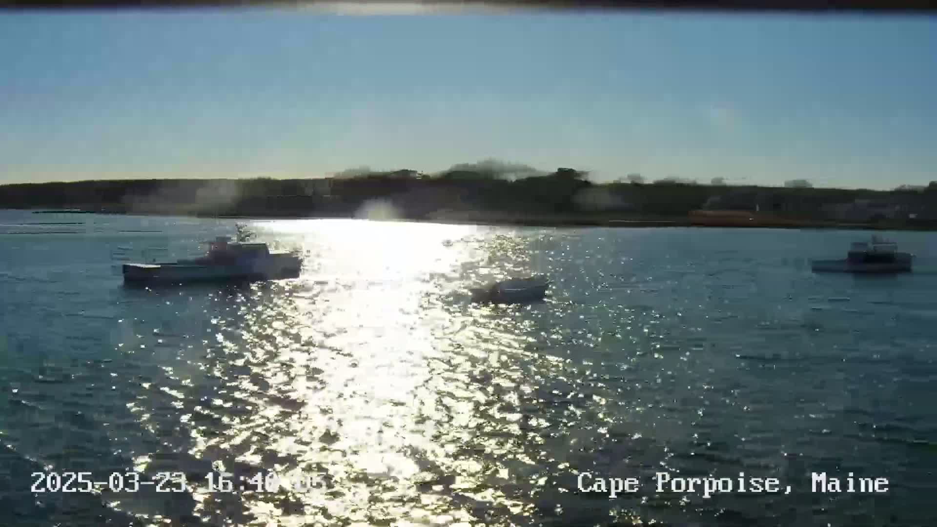 Three boats are on a sunny, sparkling body of water near a landmass.