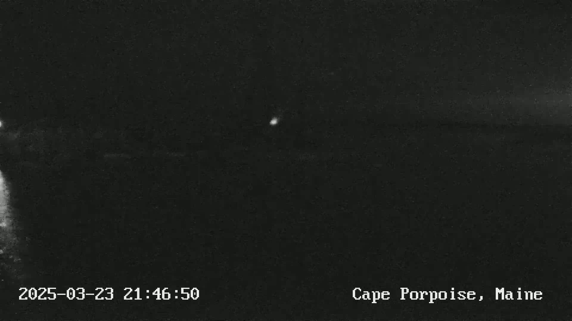 A dark, nighttime outdoor scene shows a dimly lit landscape with a single, faint light source in the distance.