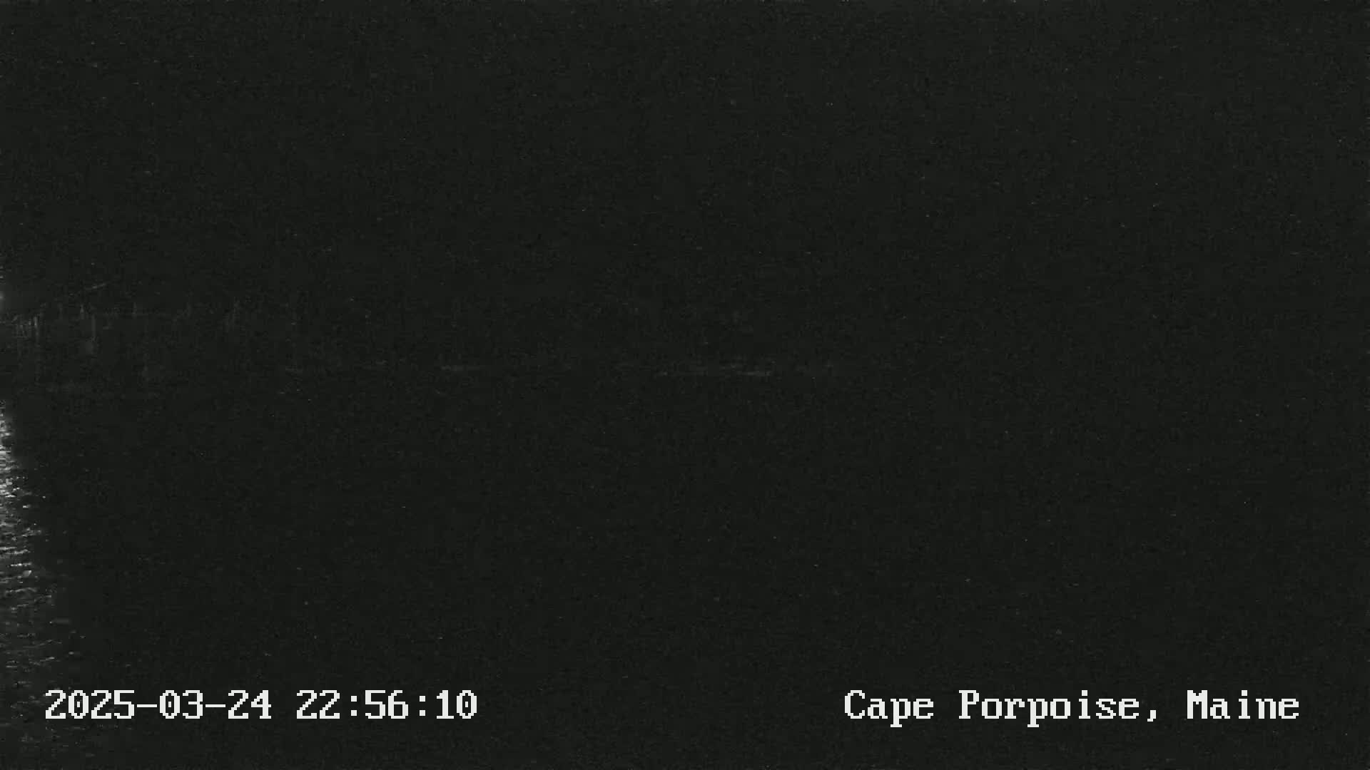 A dark, nighttime image shows a blurry view of a body of water under a dark sky.