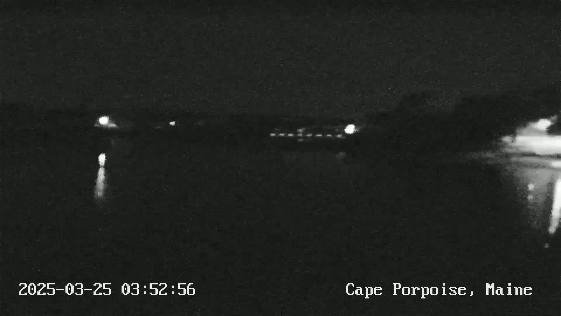A nighttime, low-light view of a dark body of water with faint lights visible in the distance.