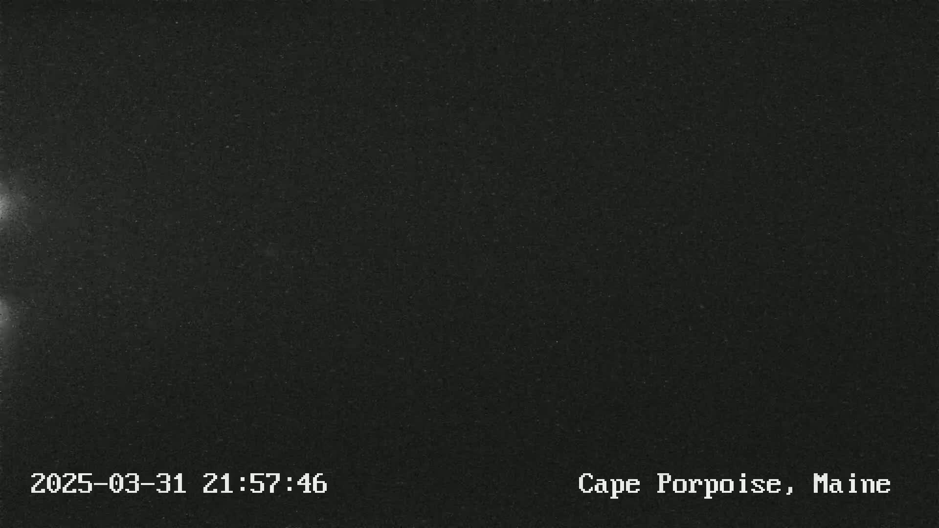 A nighttime, dark image shows a mostly black screen with some faint, brighter areas on the left side.