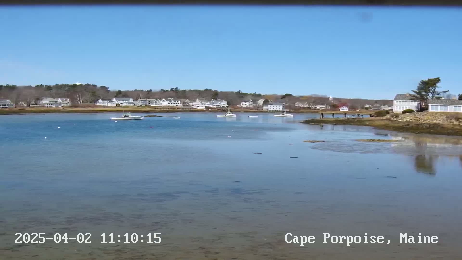 A calm, clear day reveals a coastal town with several boats in the water, and houses lining the shore.