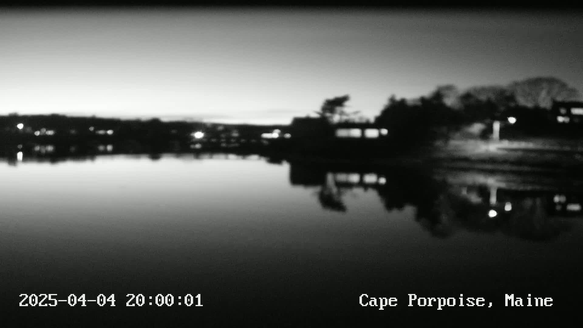 A calm body of water reflects a dark, tree-lined shoreline at twilight.