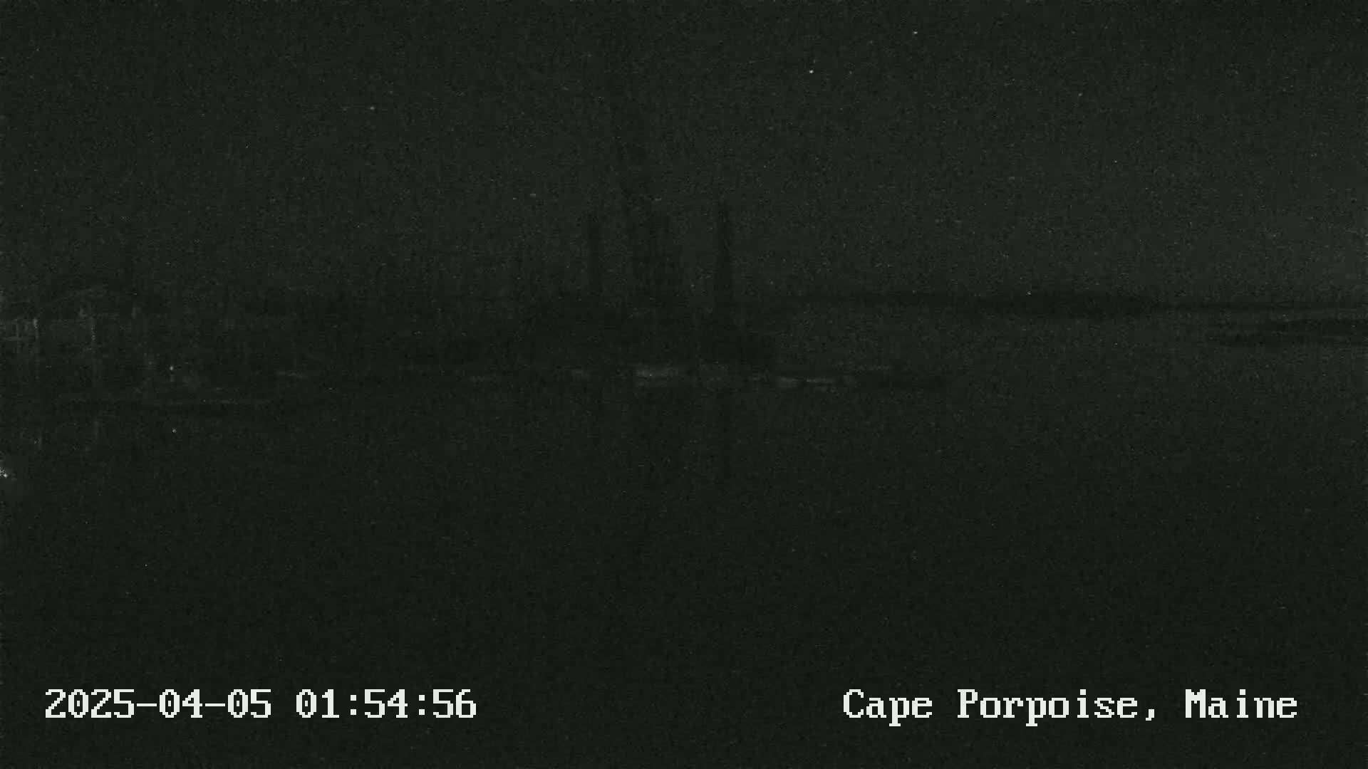 A dark, nighttime image shows a mostly indistinct body of water with a dark shoreline in the distance.
