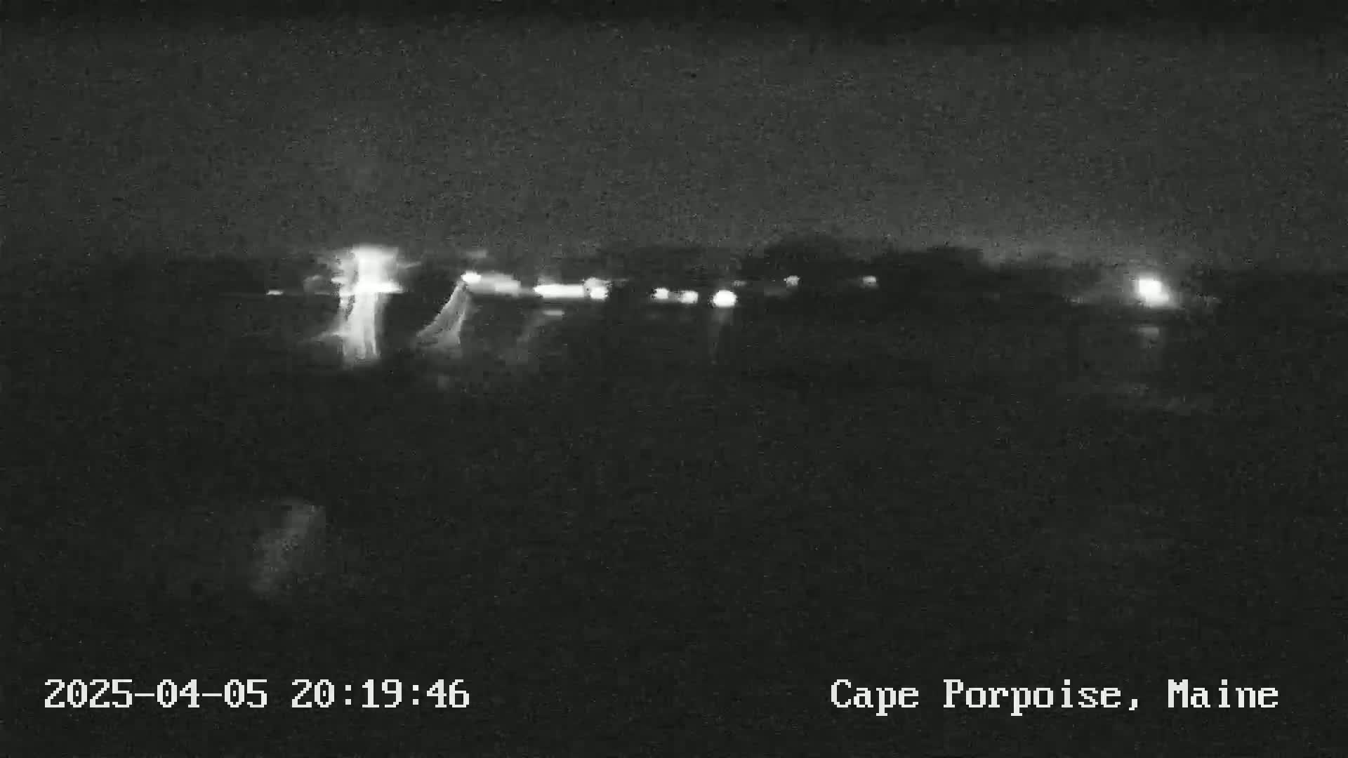 A nighttime, low-light view shows a dark landscape with a few faint lights in the distance.