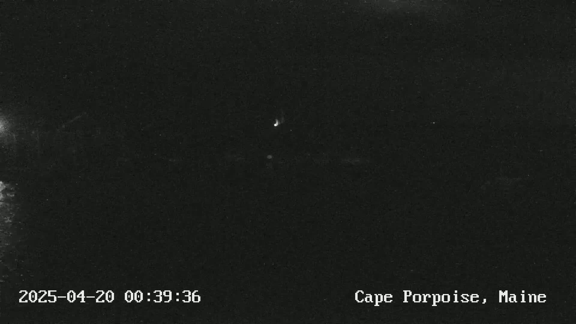 A dark, nighttime image shows a few faint lights in the distance under a clear sky.