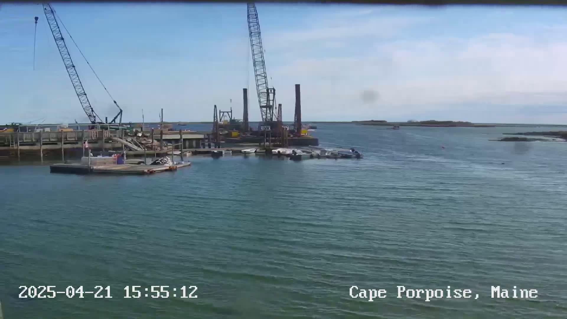 Two large cranes and several boats are situated in a harbor under a partly cloudy sky.