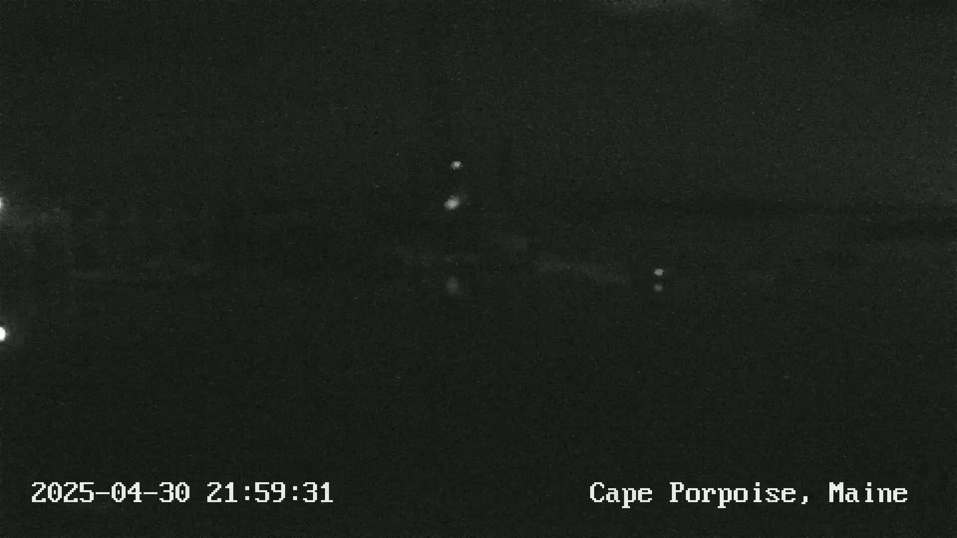 A nighttime, low-light image shows a dark, possibly water-based scene with a few faint, distant lights.