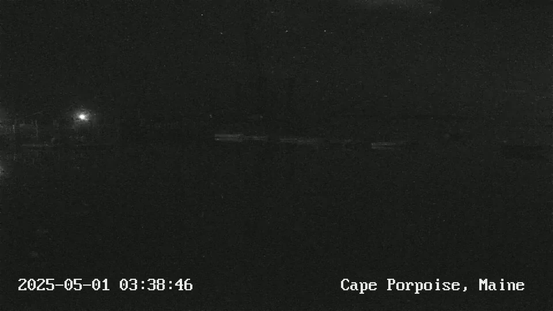 A dark, nighttime scene shows a dimly lit area, possibly near water, under a clear, starless sky.