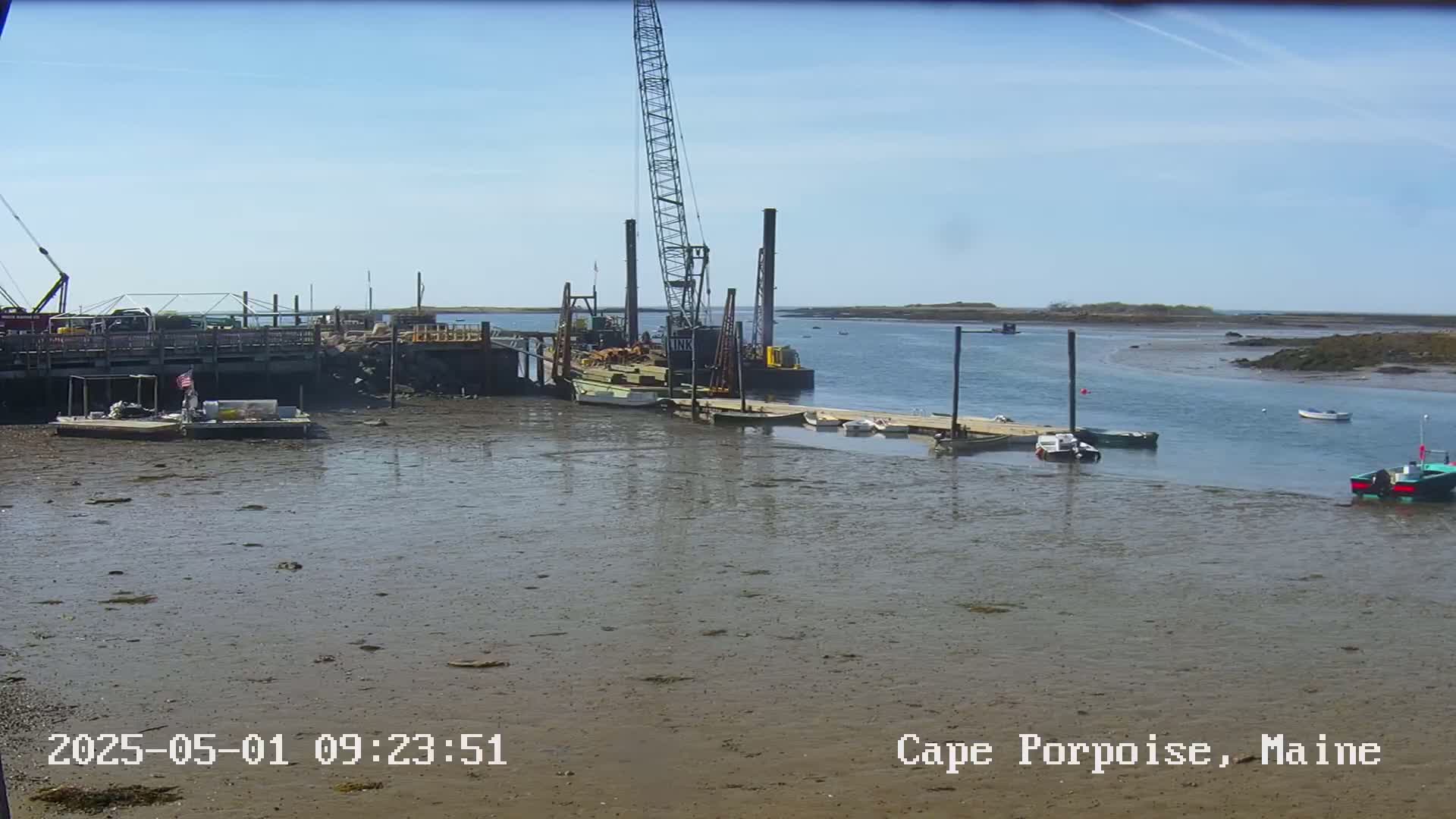 A large crane sits on a barge in a harbor at low tide under a clear sky.