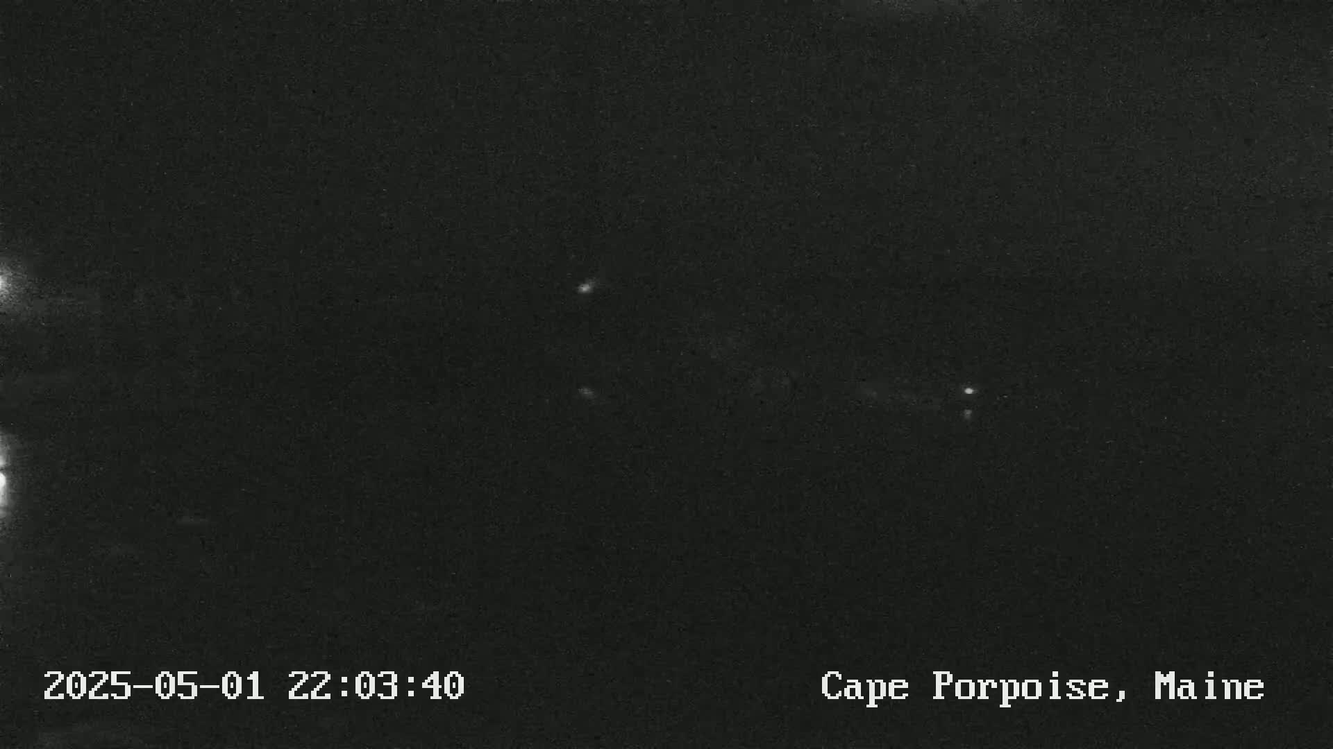 A nighttime, low-light image shows a dark scene with a few faint lights visible in the distance.