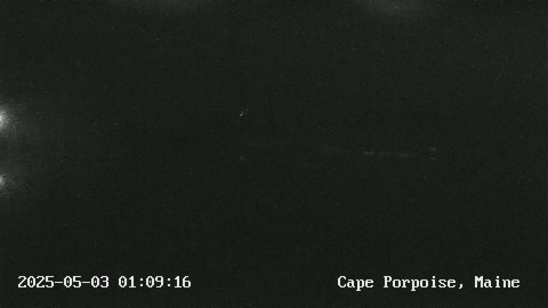 A nighttime, dark image shows a mostly black sky with a few faint, bright spots.