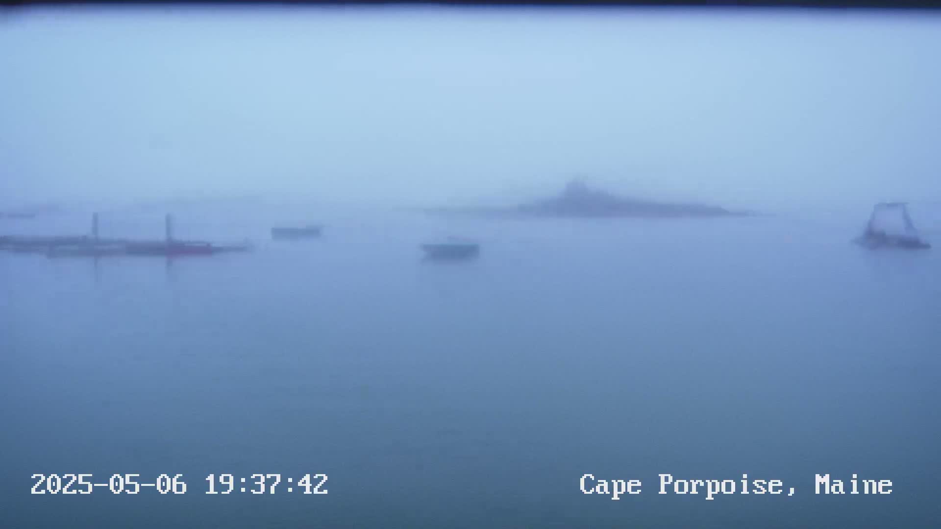 Several boats are visible on a foggy body of water with a hazy landmass in the background.