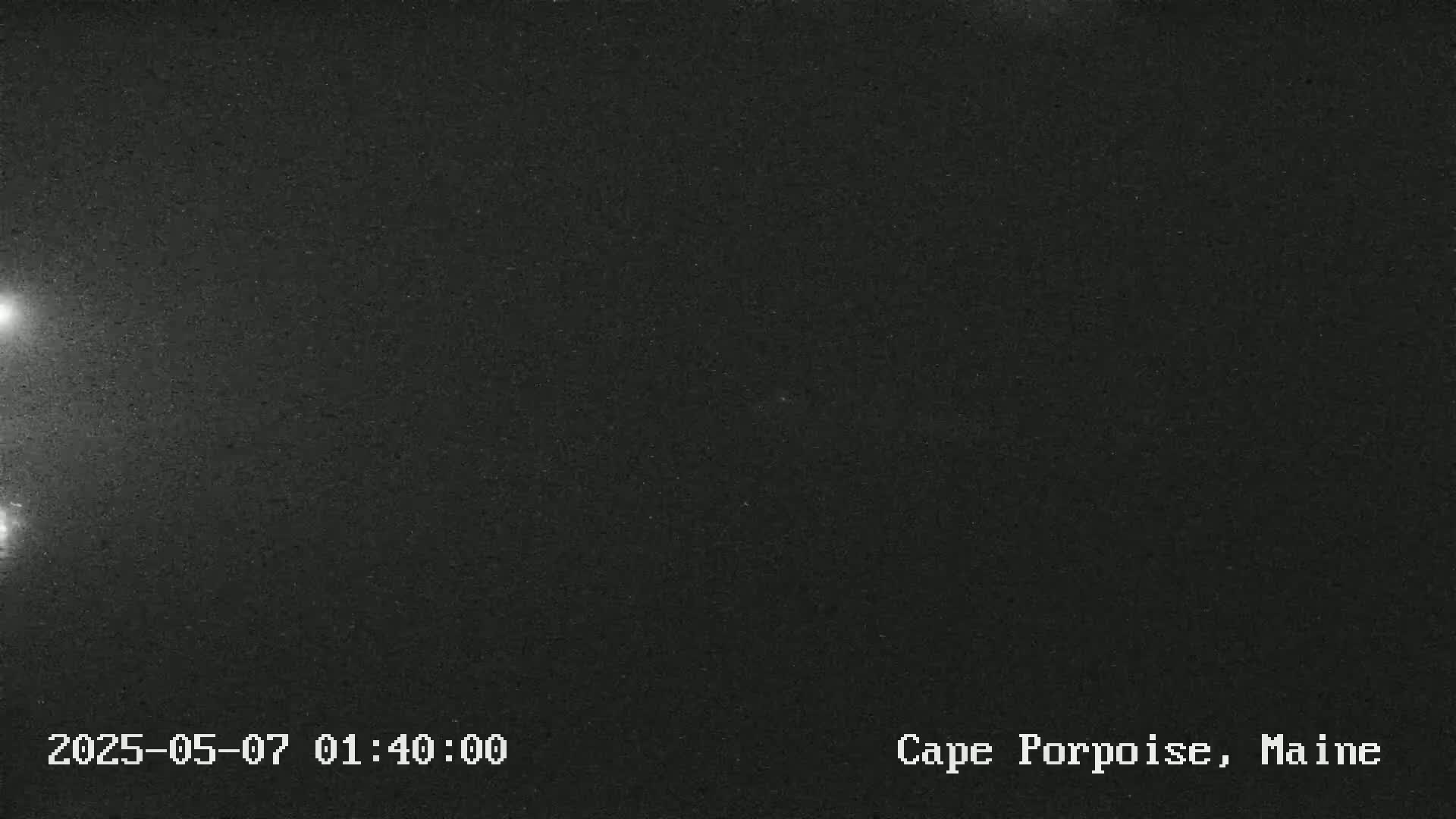 A nighttime, low-light image shows a dark sky with two bright lights on the left.