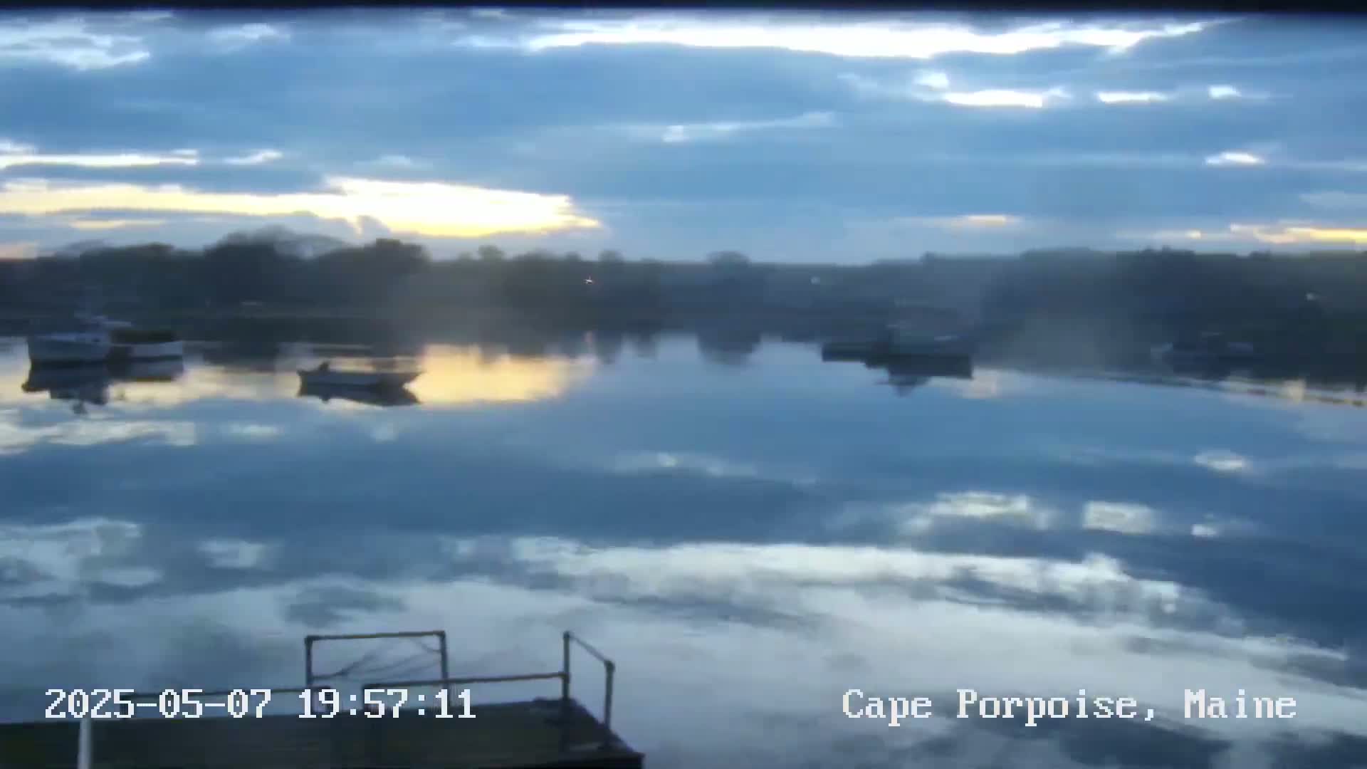 Several small boats are moored in a calm body of water under a partly cloudy, dusky sky.