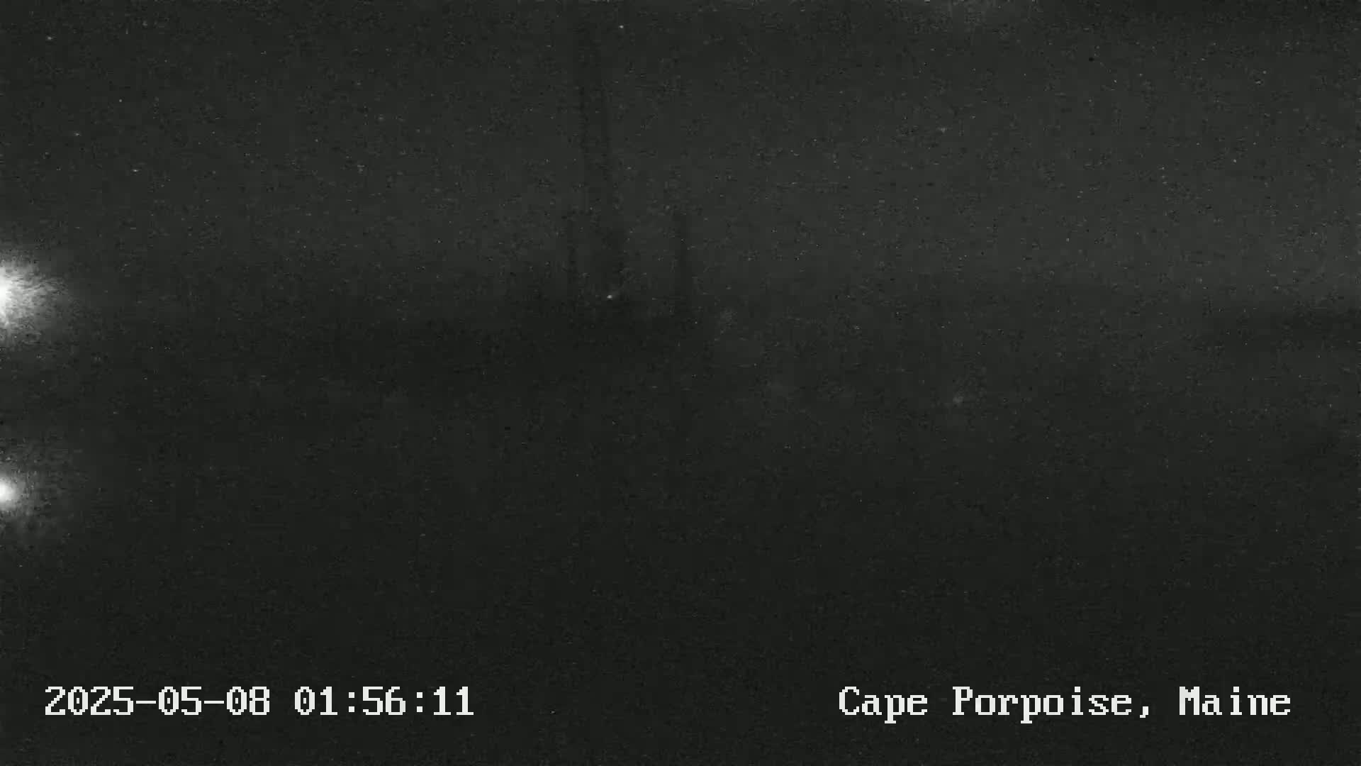 A dark, nighttime outdoor scene shows a blurry, indistinct view with two bright lights in the lower left corner.