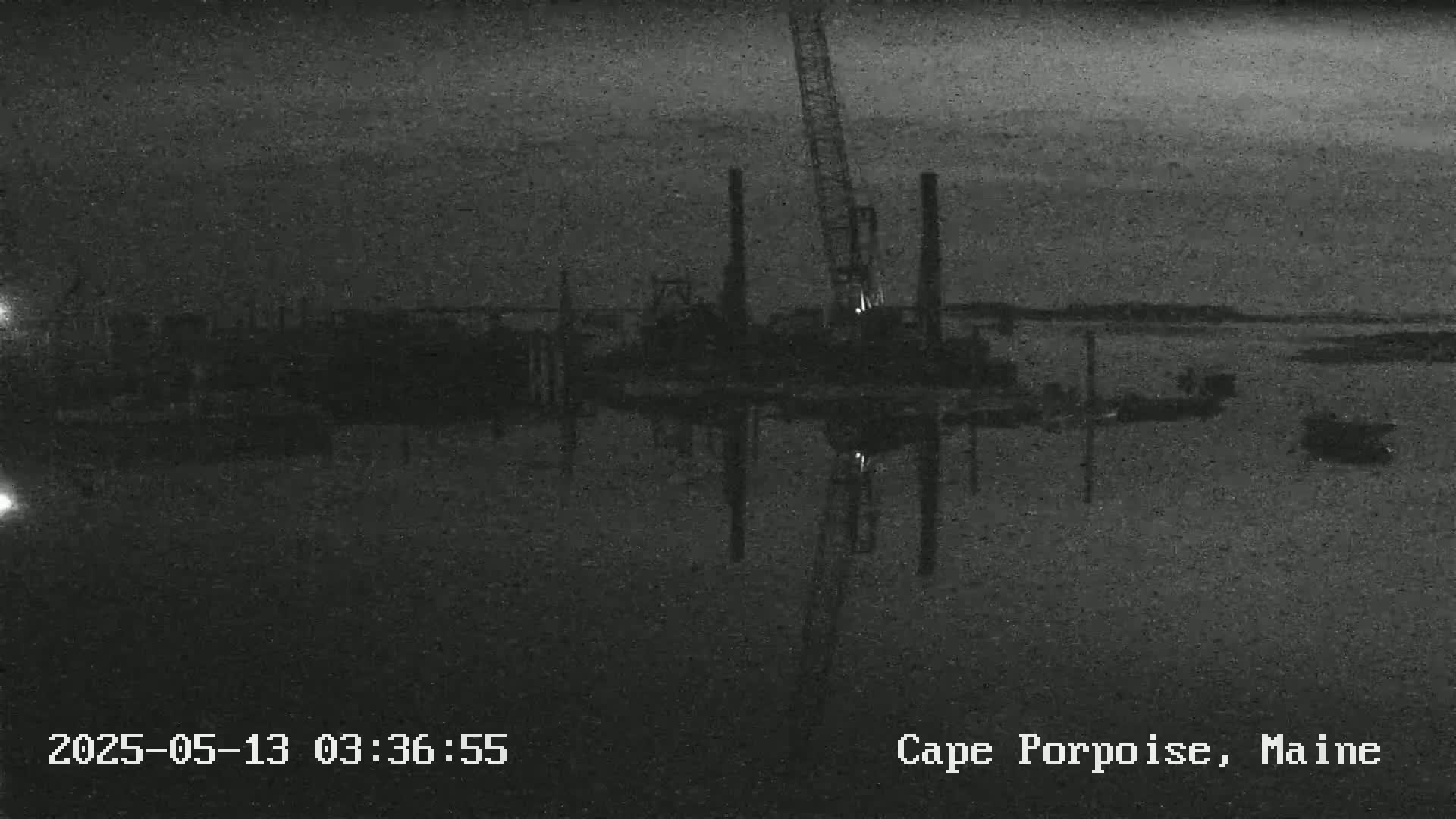 A nighttime, low-light image shows a construction site with machinery near a body of water.