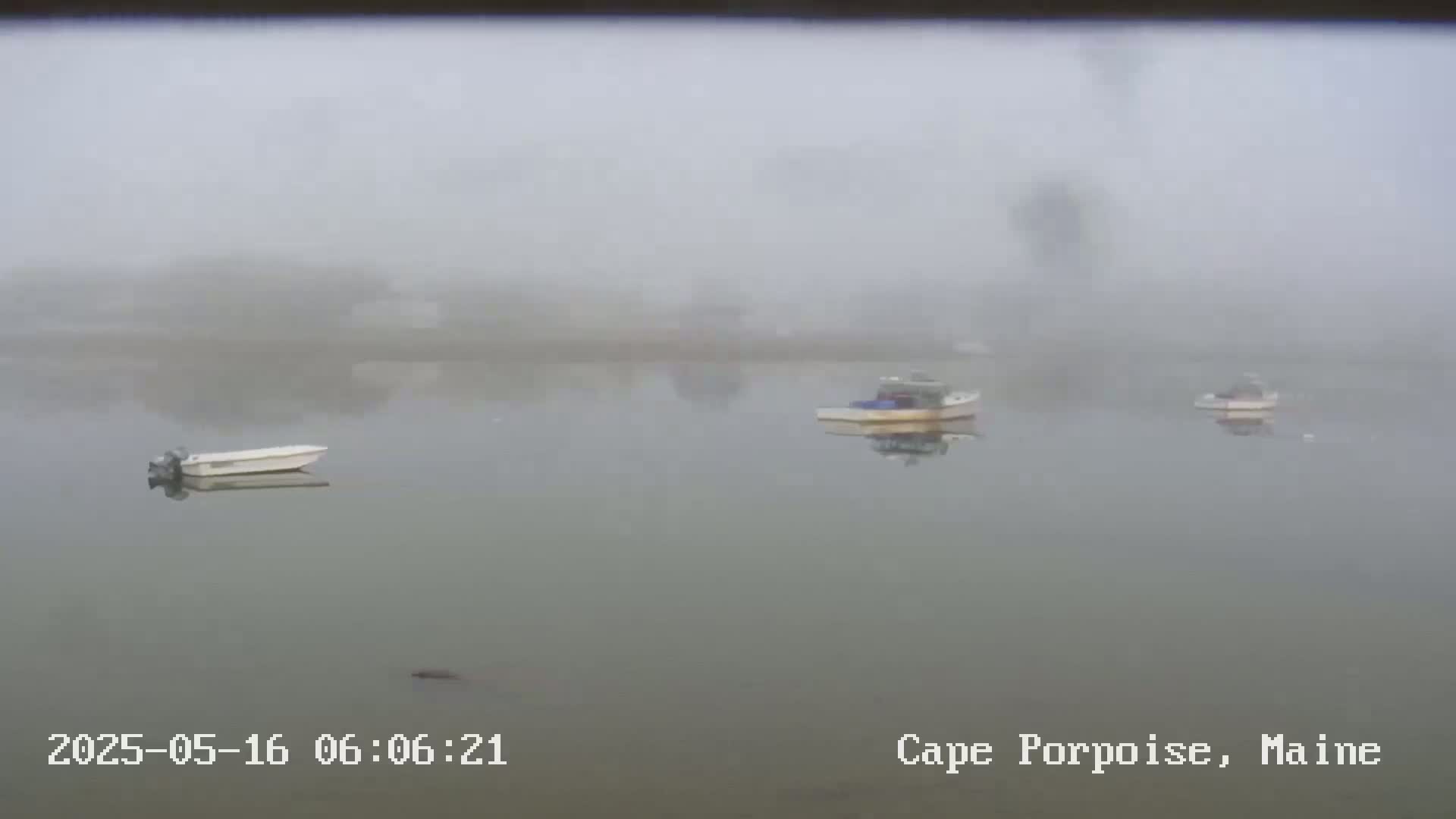 Three small boats are moored in a calm, foggy body of water.