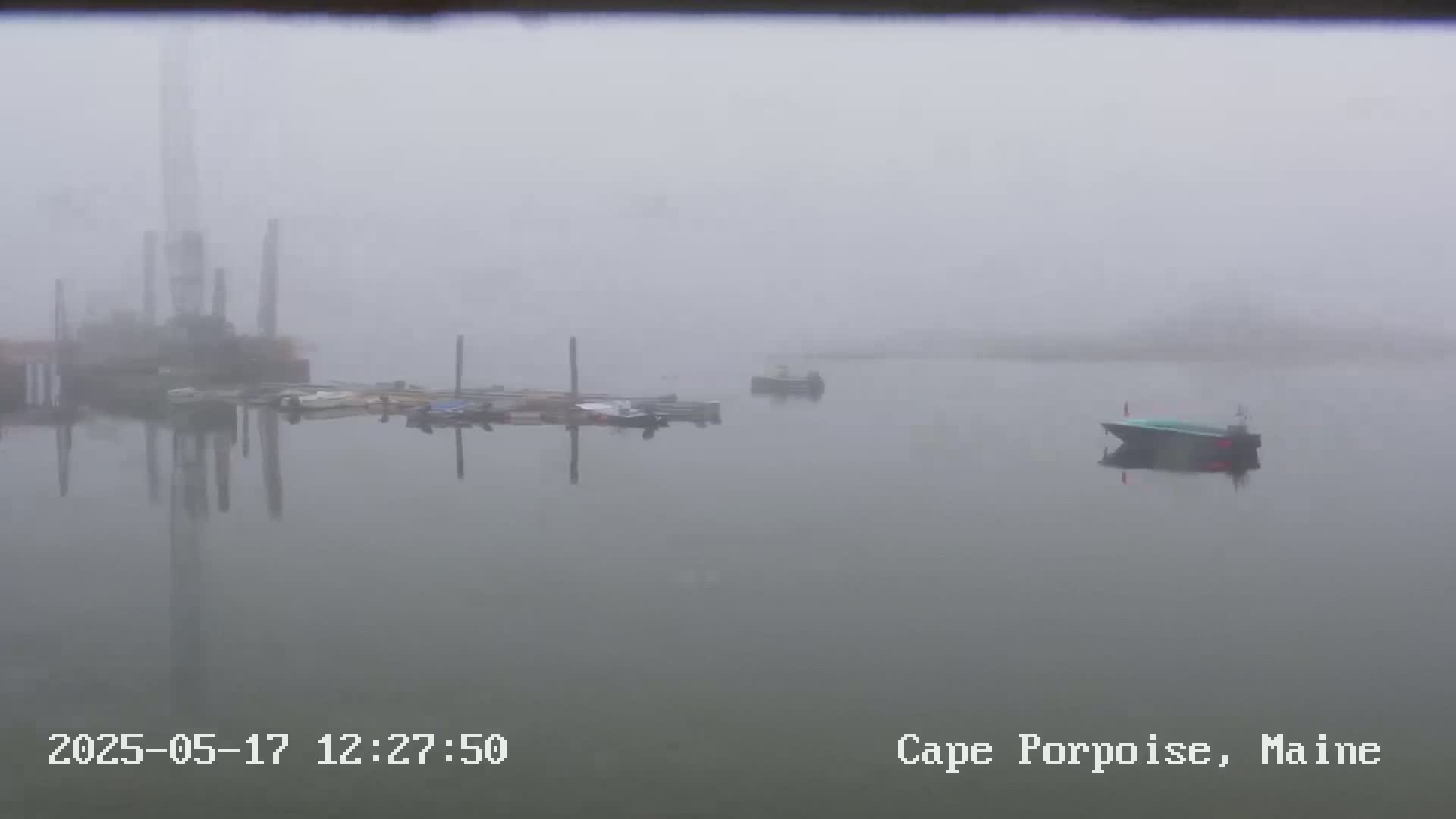 A foggy harbor scene shows several boats moored at a dock, with one boat further out in the water.