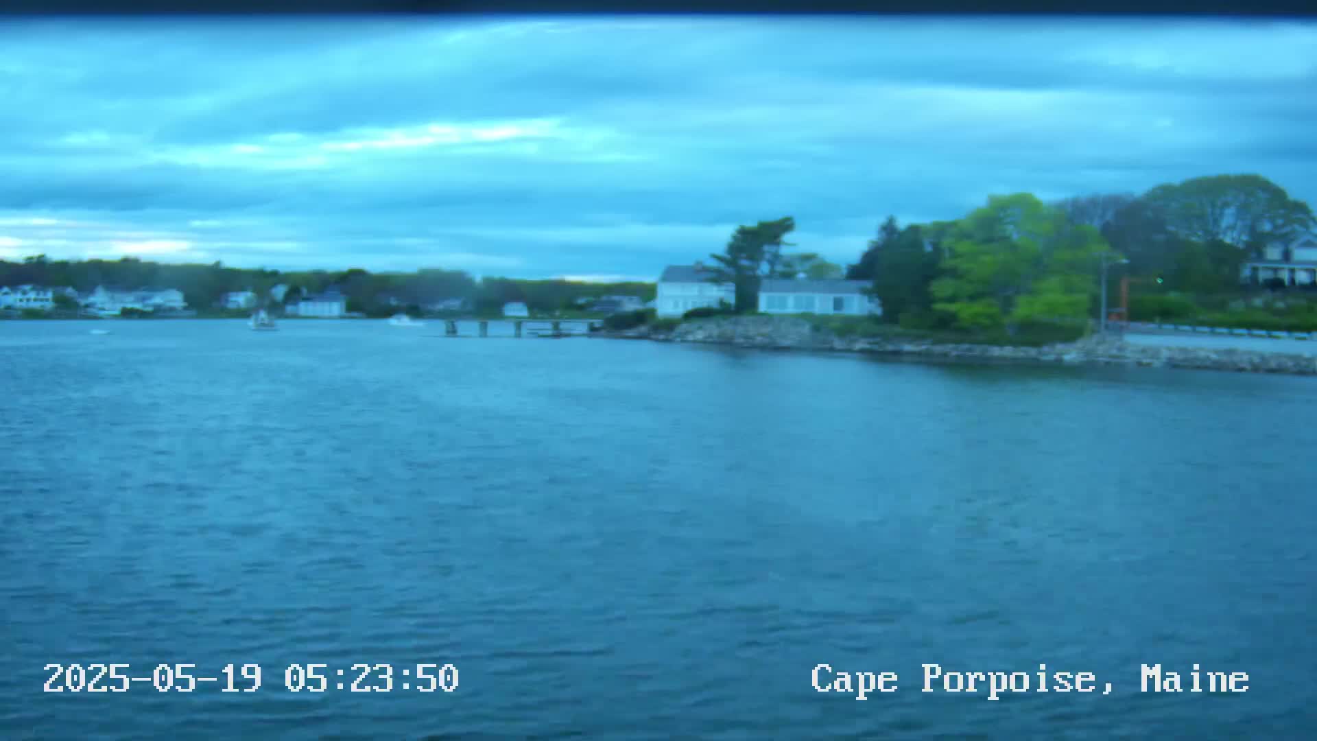 A body of water shows a shoreline with houses and trees under a mostly cloudy, dusky sky.