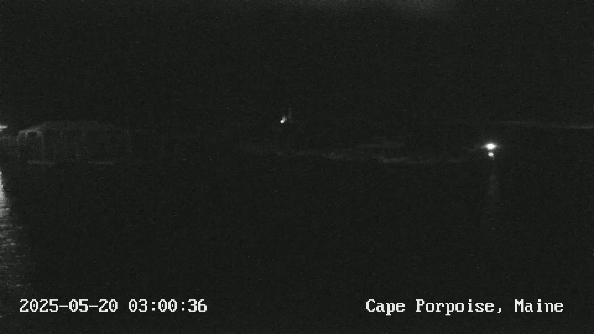 A nighttime, low-light view of a dark body of water with faint lights visible on the far shore.