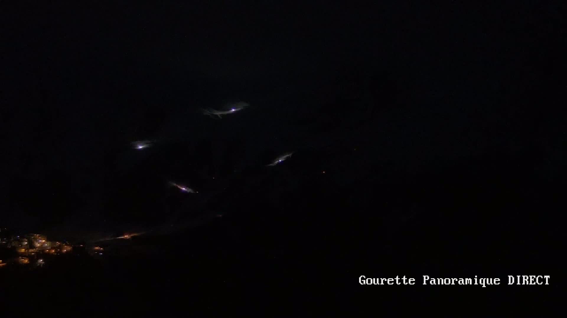 Several streaks of light appear in a dark night sky above a dimly lit town.