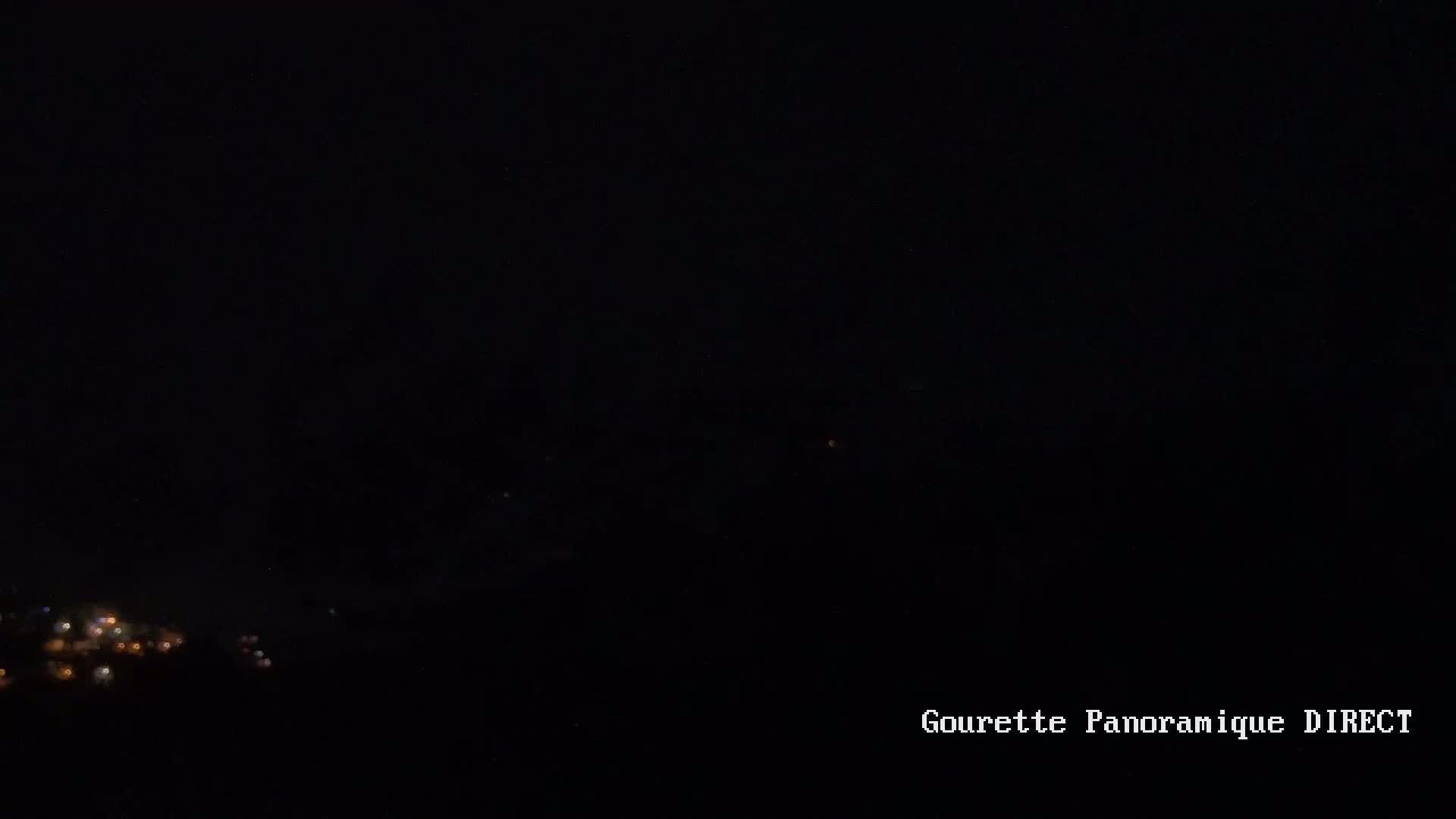 A nighttime long shot shows a cluster of dim lights in the lower left corner, likely a town or village, against a completely dark sky.