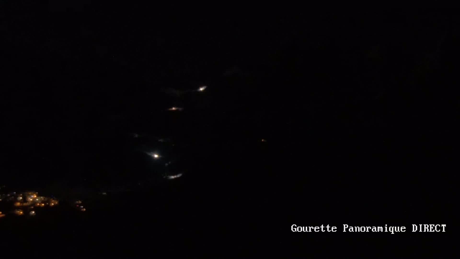 A nighttime view shows several bright lights in the sky above a small cluster of dim lights on the ground.