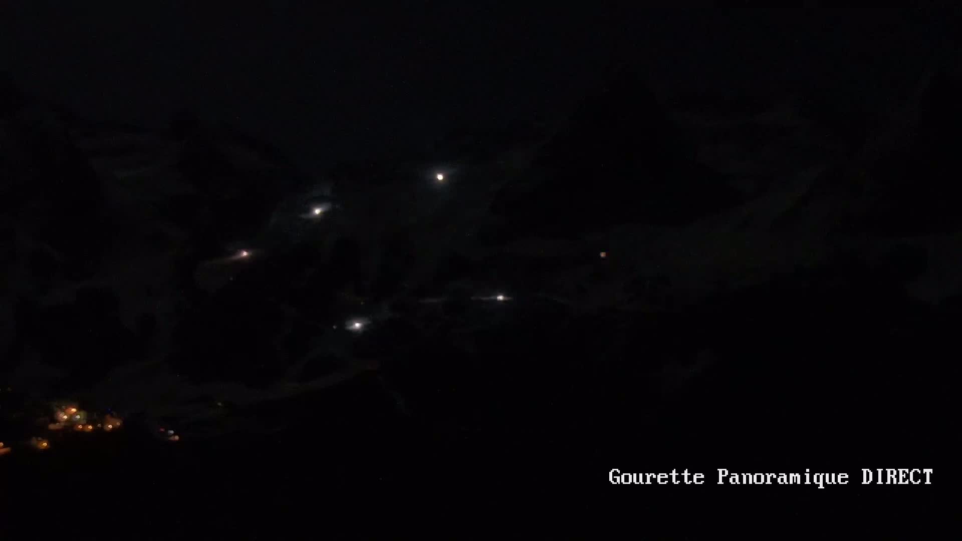 Several bright lights are visible in the night sky above a dark landscape with a few small lights in the bottom left corner.