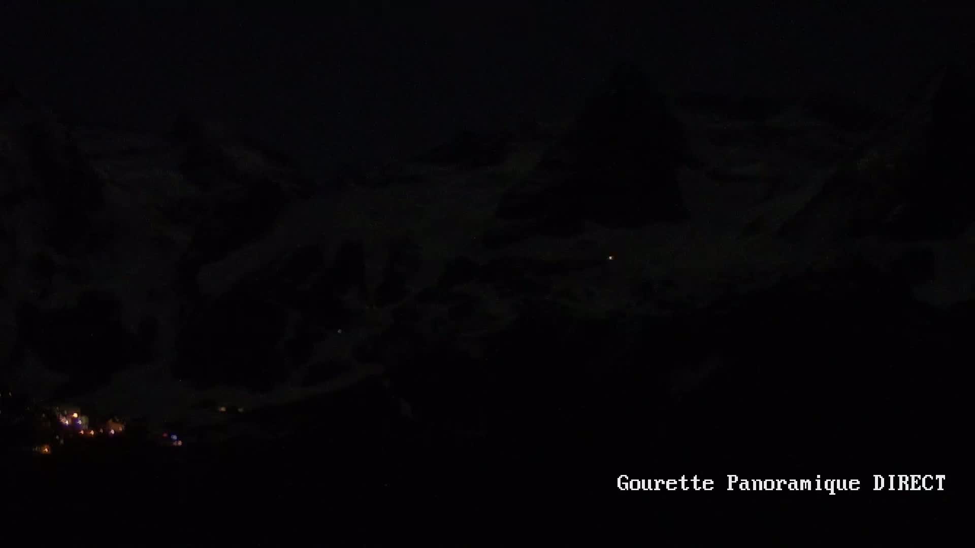 A nighttime view of dimly lit snow-covered mountains and a small village below.