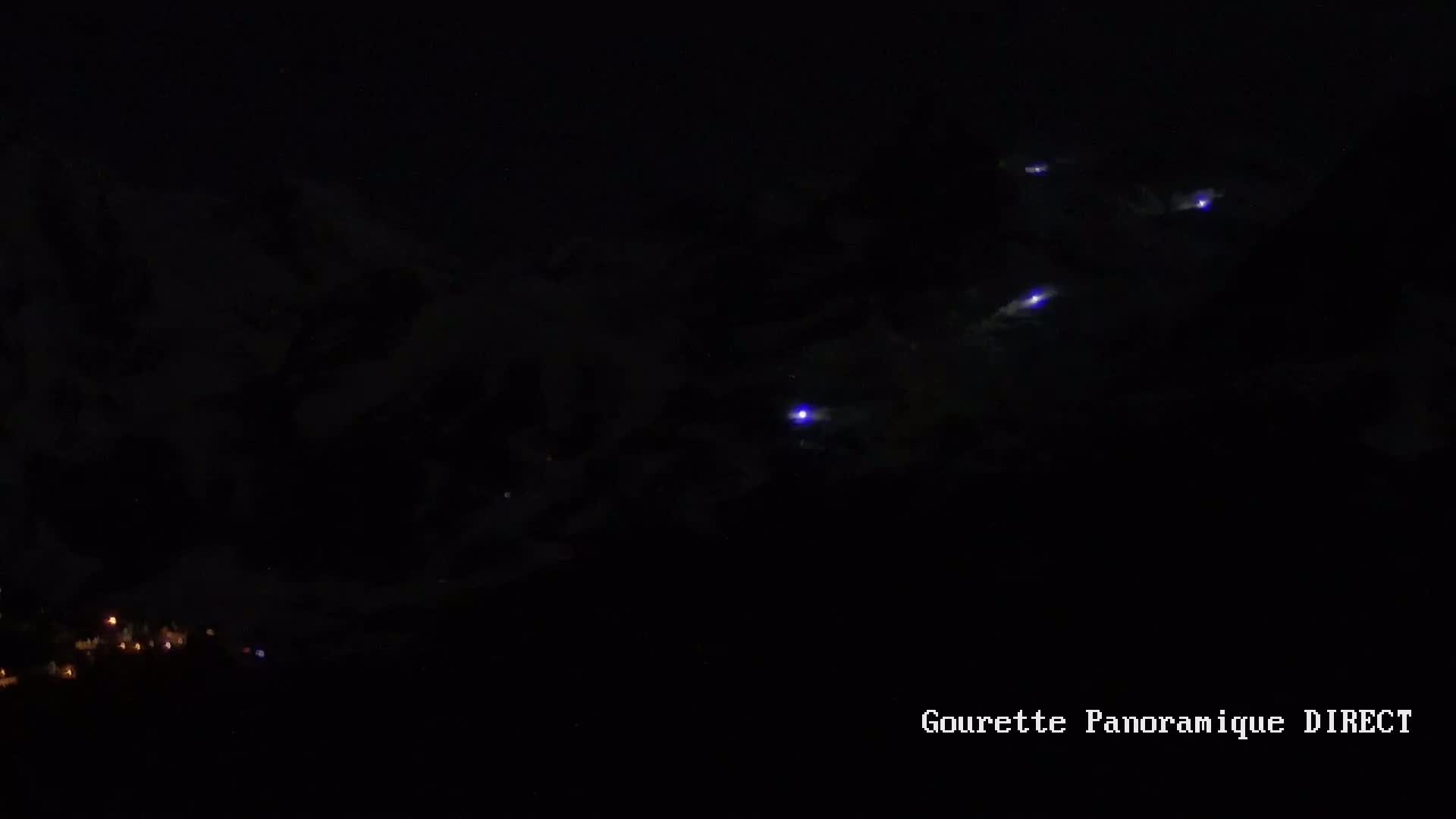 Several faint purple lights appear in a dark night sky above a dark landscape with small, distant lights below.