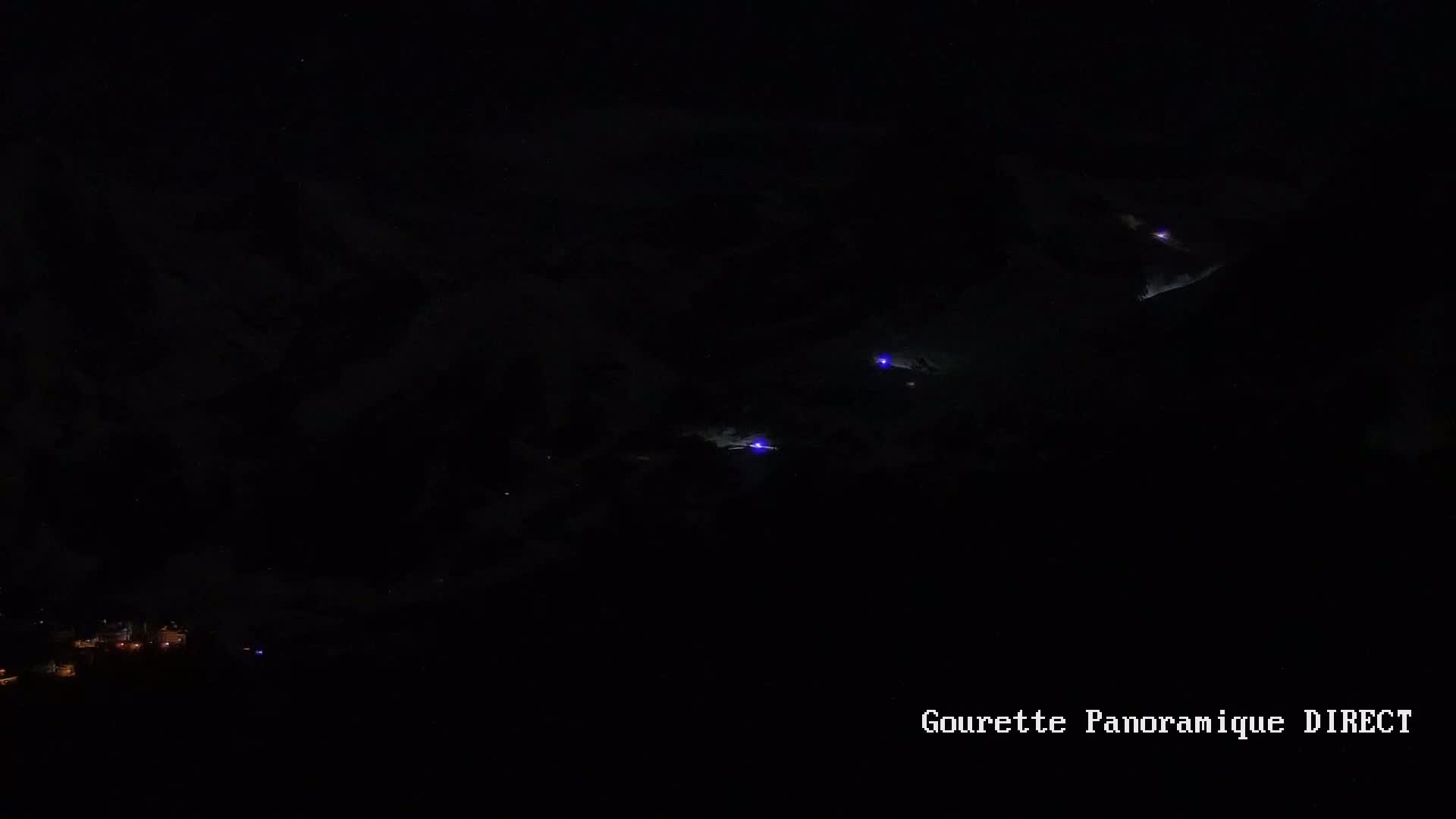 A nighttime long shot shows several small, faint purple lights in the dark sky above a dimly lit town.