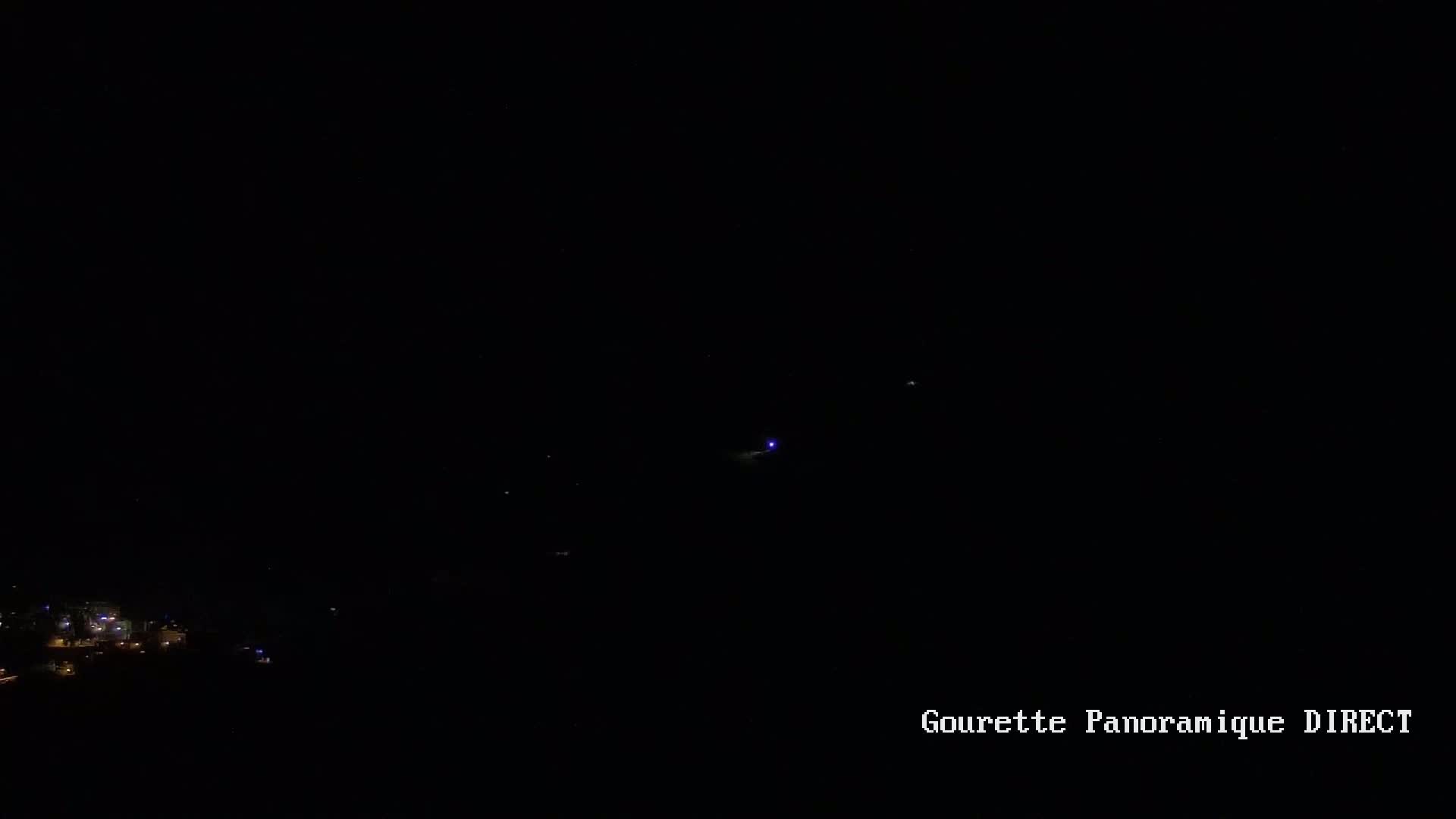 A nighttime long shot shows a few distant lights below a dark sky with a small cluster of brighter lights in the middle distance.