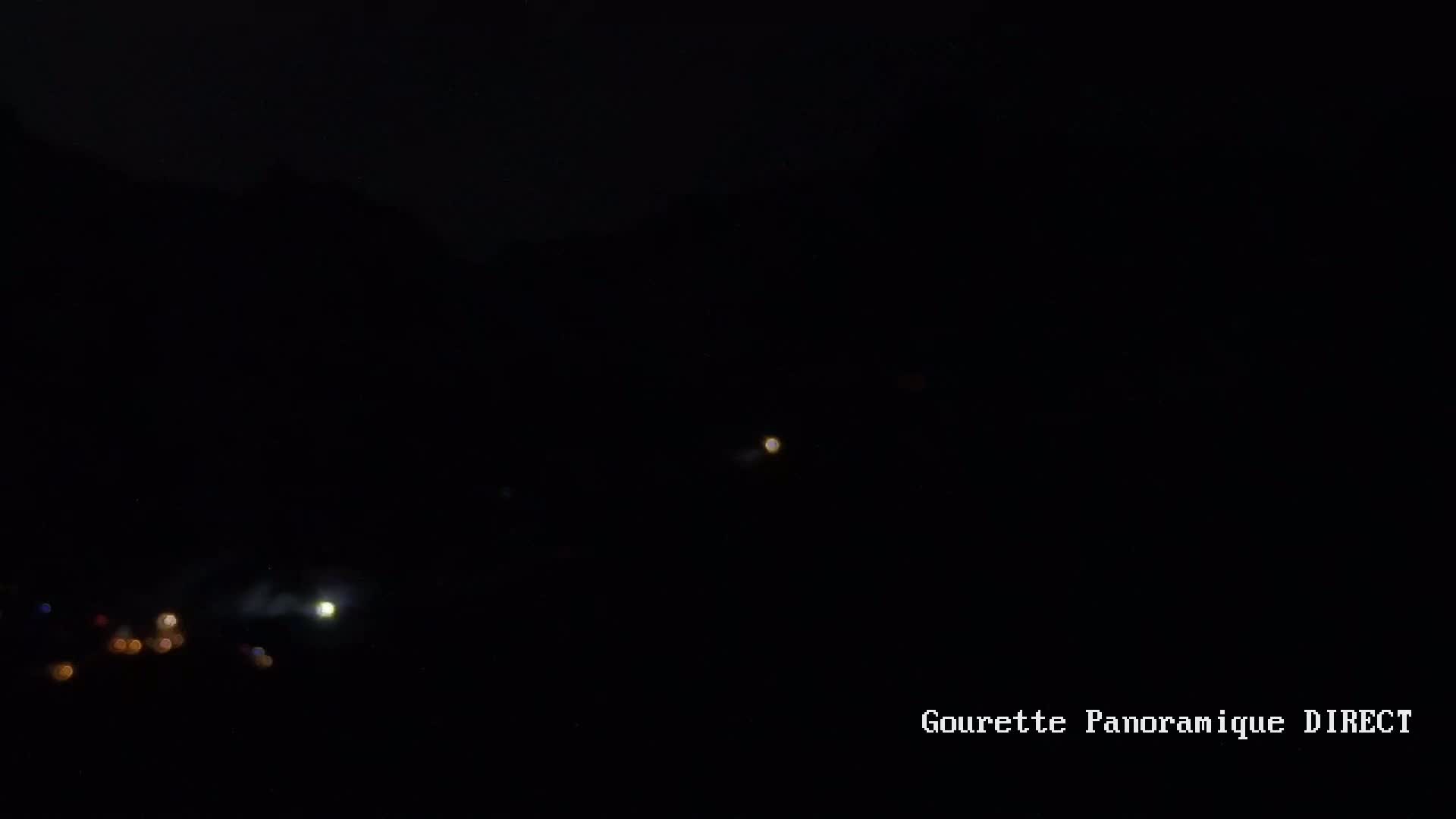 A dark nighttime scene shows a few distant lights and what appears to be a bright light source, possibly a moon, in the sky.