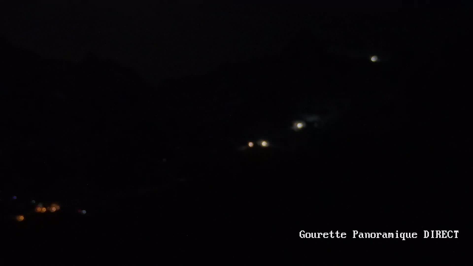 Several blurry lights are visible in the night sky above a dark landscape with a few faint lights in the lower left corner.