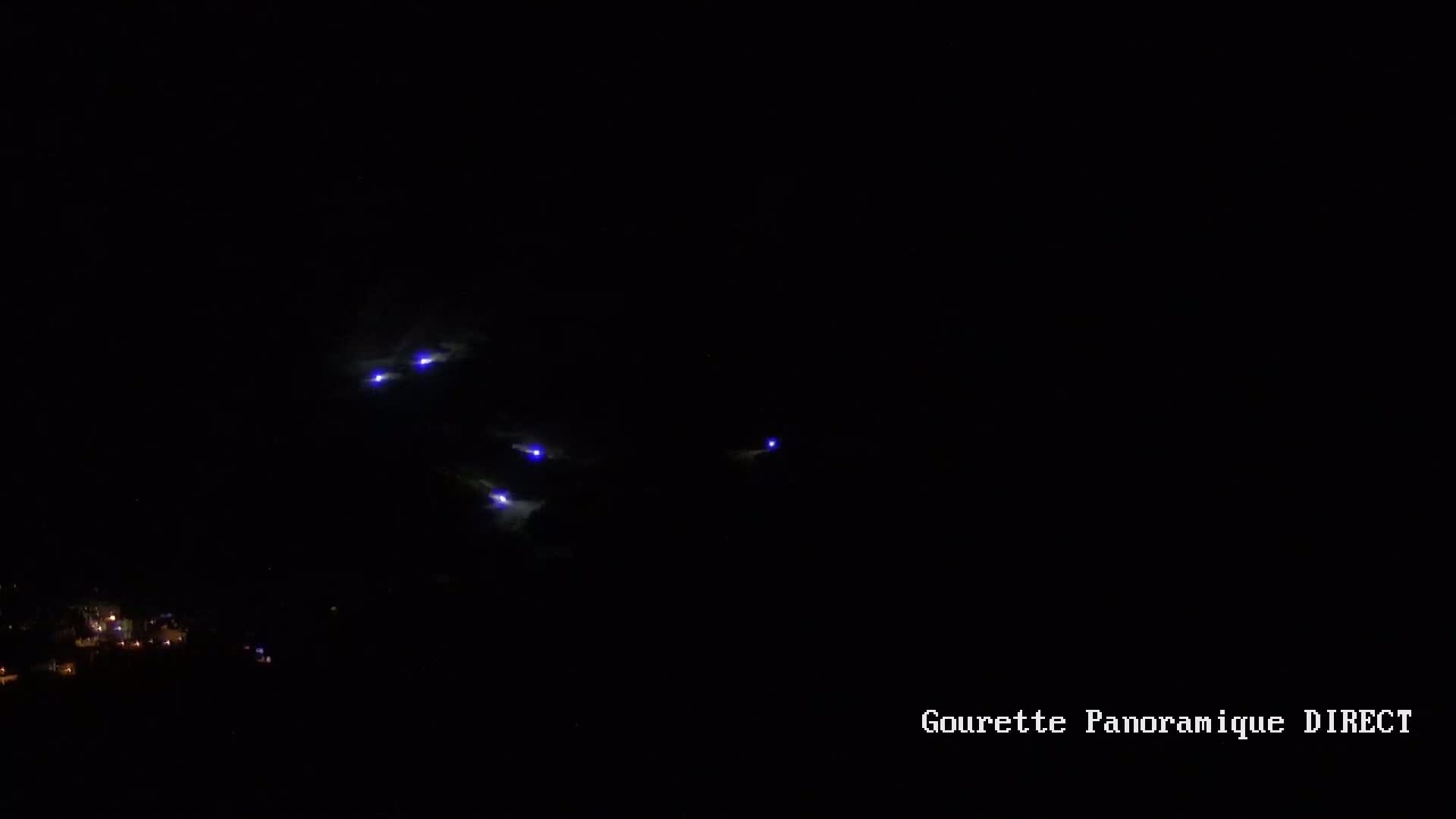 Several small, faint blue lights are visible in the nighttime sky above a dimly lit town.
