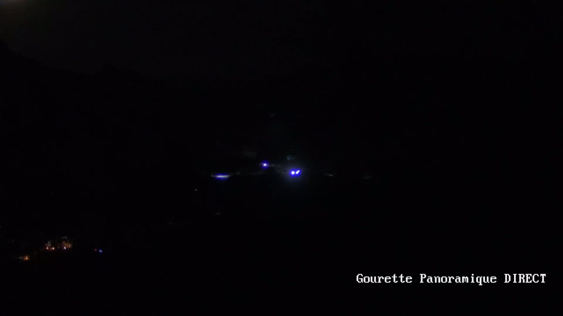 A low-light image shows a distant aircraft with its navigation lights illuminated at night.