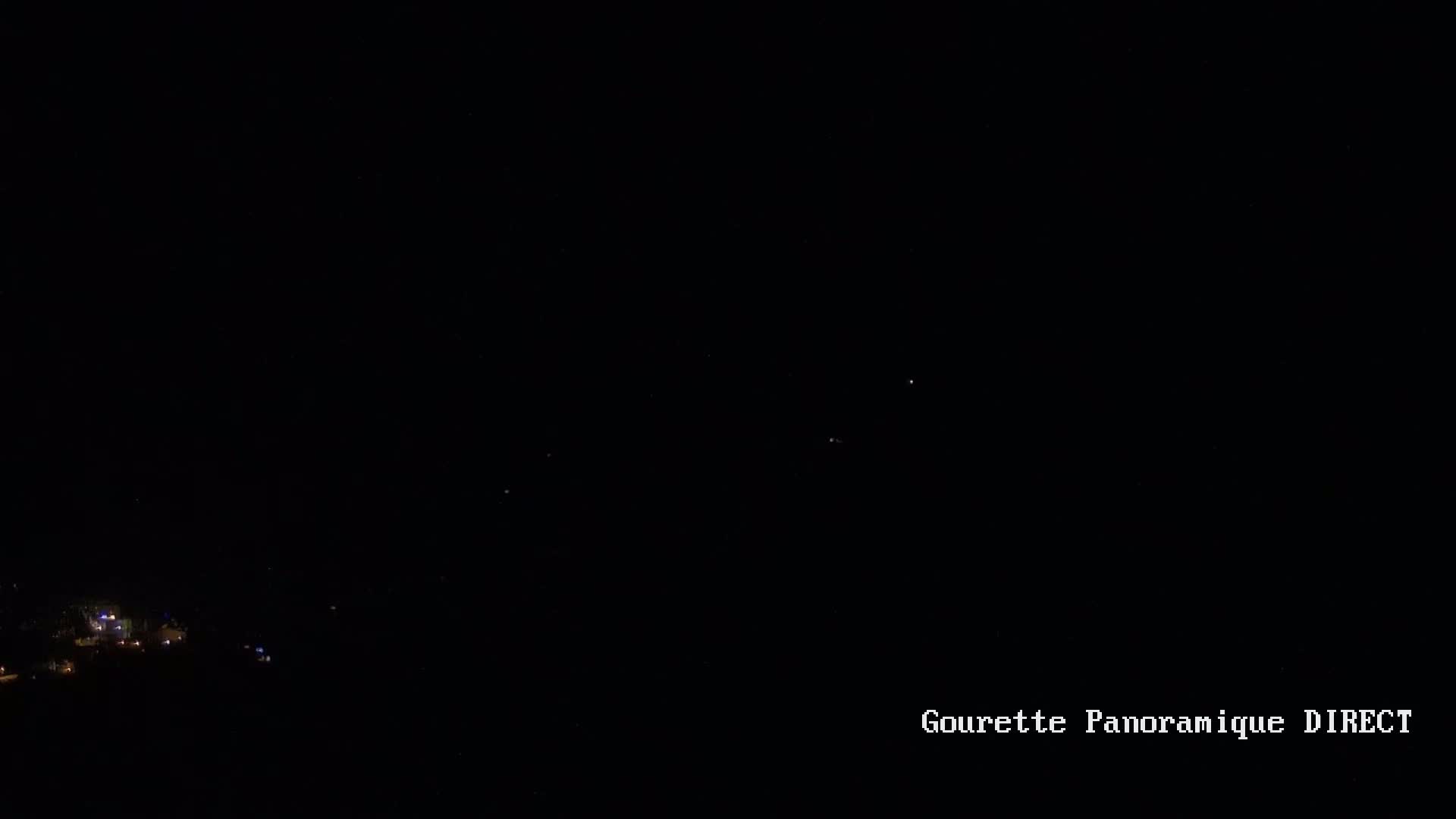 A nighttime long shot shows a few faint lights in the distance below a dark sky speckled with stars.