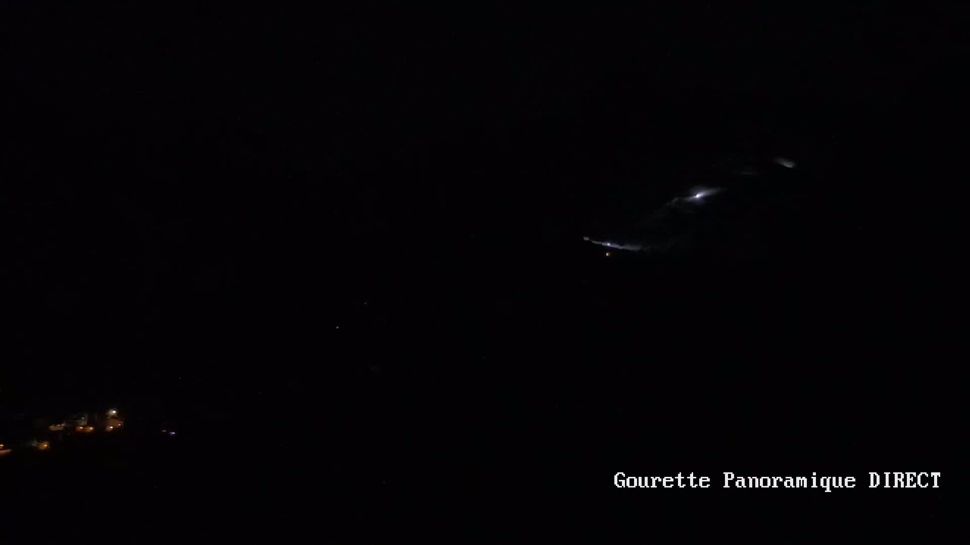 A nighttime long shot shows a faintly illuminated cloud formation above a dark landscape with a few small, distant lights.
