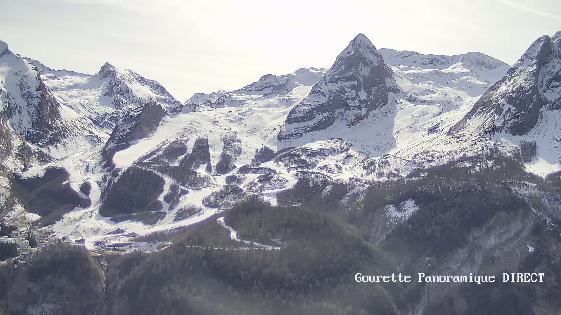 A snow-covered mountain range with ski runs is visible under a bright, sunny sky.