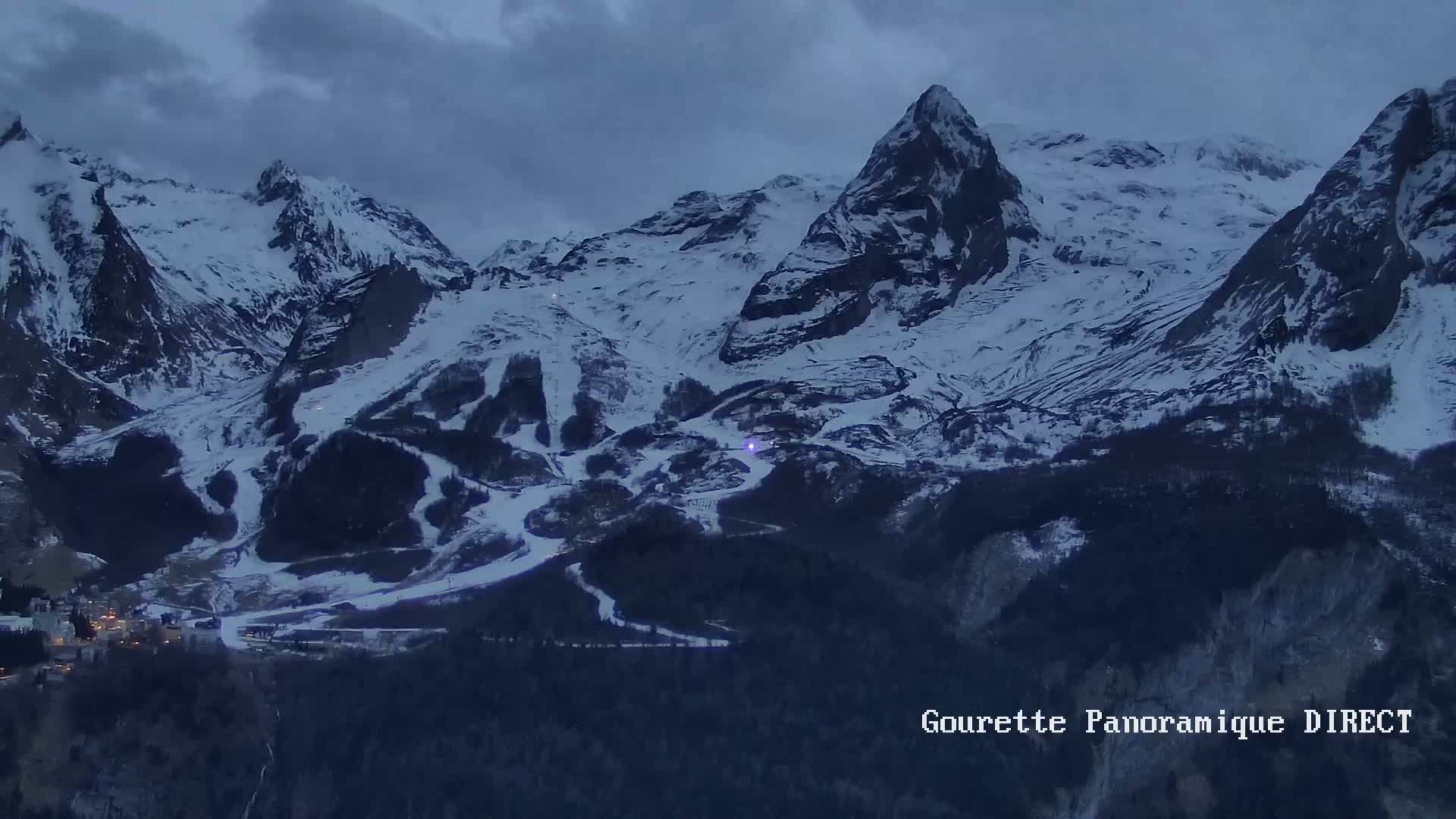 A snow-covered mountain range with ski slopes is visible under a cloudy, dark sky.