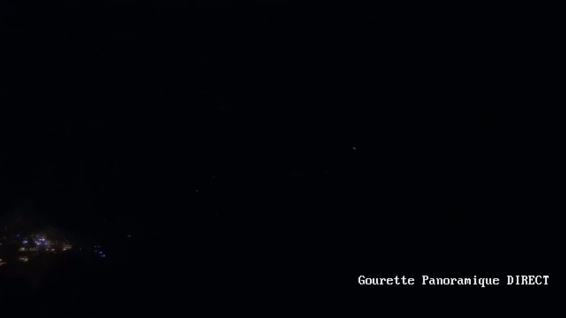 A nighttime long shot shows a small cluster of faint lights in the lower left corner against a mostly dark sky.