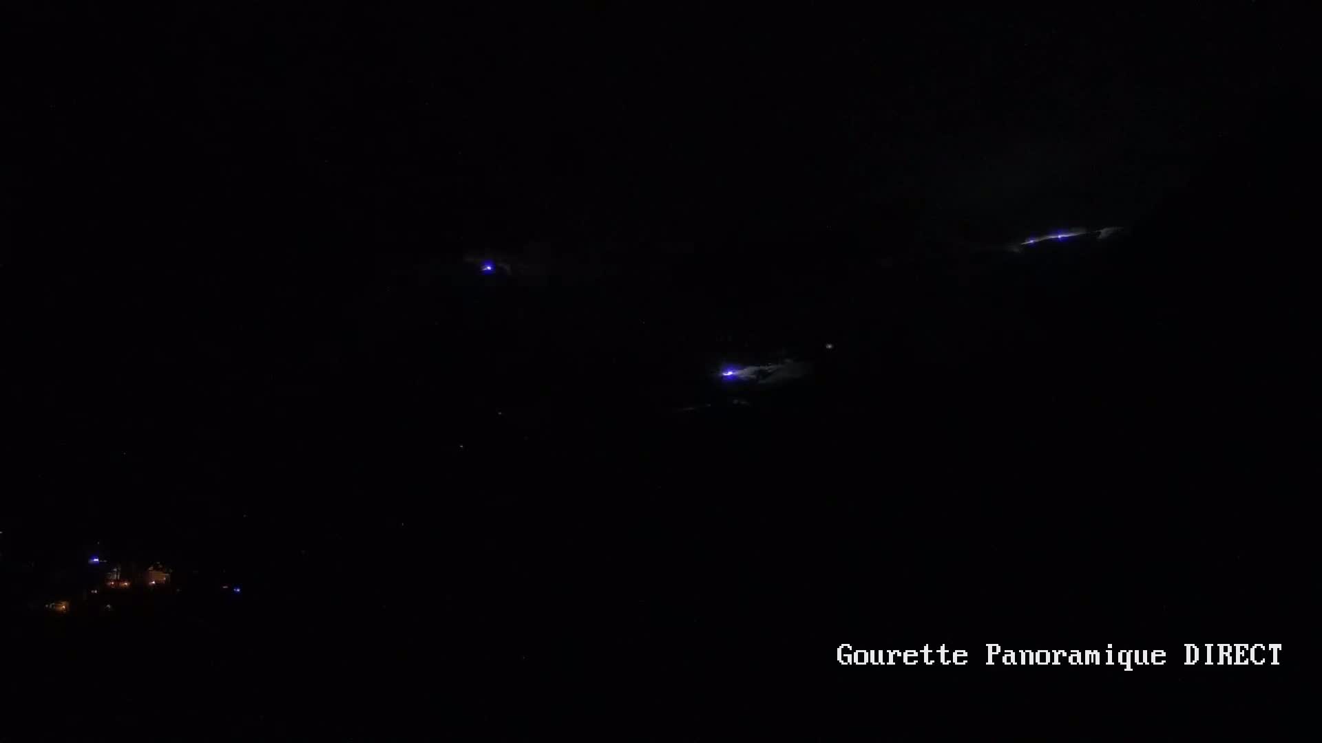 Several purplish-blue lightning strikes illuminate a dark, nighttime sky above a dimly lit landscape.