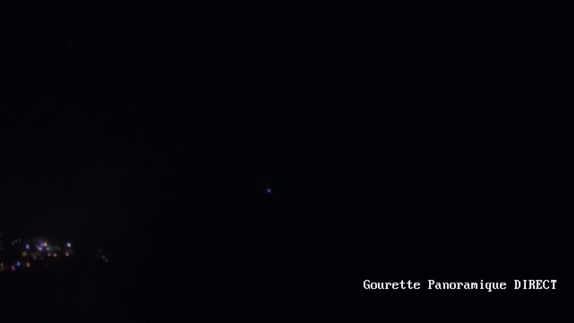 A dark night sky shows a cluster of distant lights below and a single bright light in the center.